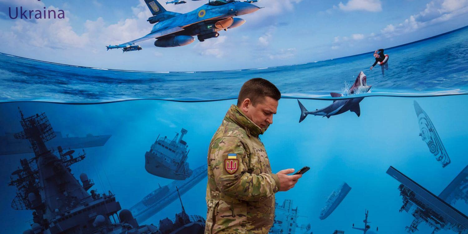 En ukrainsk soldat passerar en stor illustration som ska visa sänkta ryska örlogsfartyg och en Vladimir Putin i sjönöd, i Kiev den 15 mars i år.
