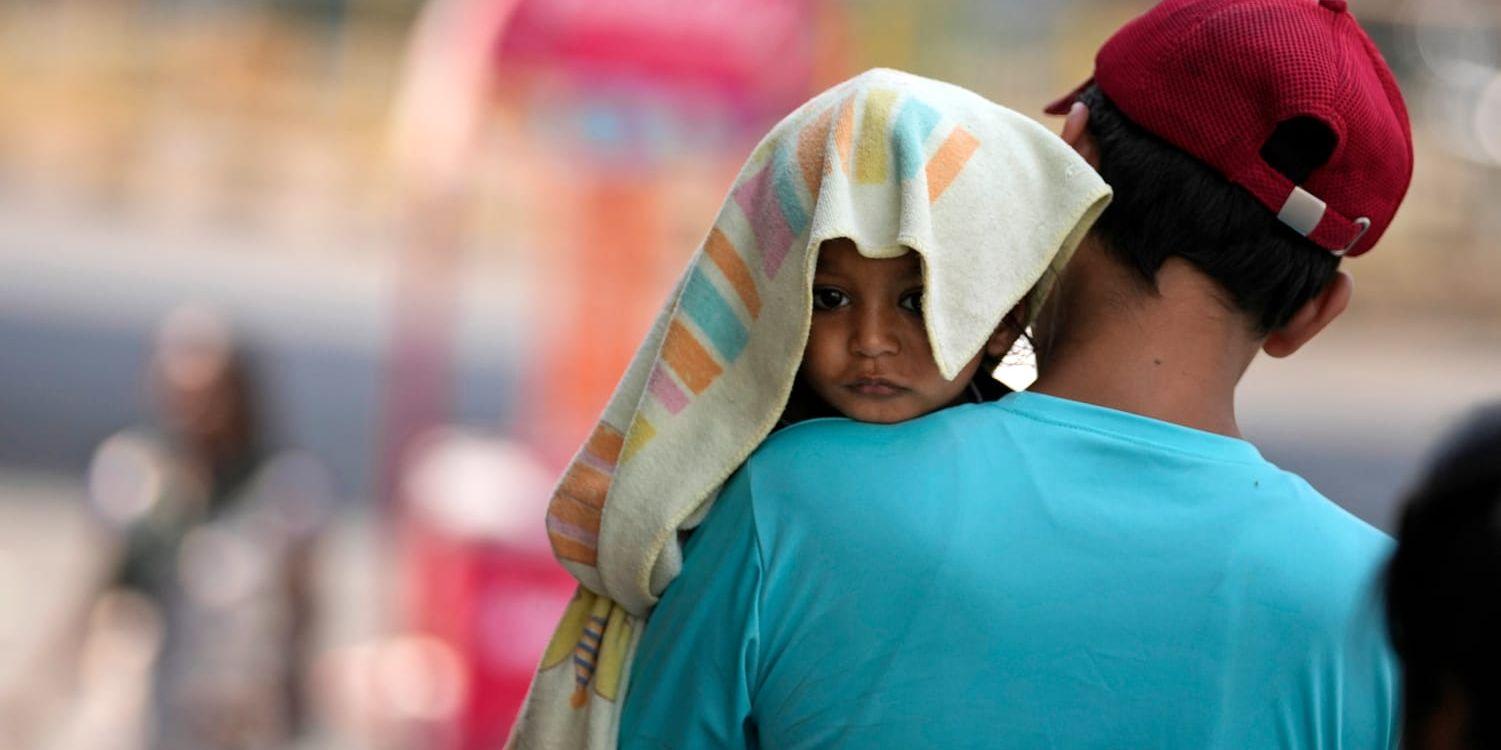 En man bär ett barn med huvudet täckt av en handduk som skydd mot värmen i Jammu, Indien. En månadslång värmebölja över stora delar av Indien har lett till 100 dödsfall och över 40 000 misstänkta fall av värmeslag. Bild från den 2 juni.