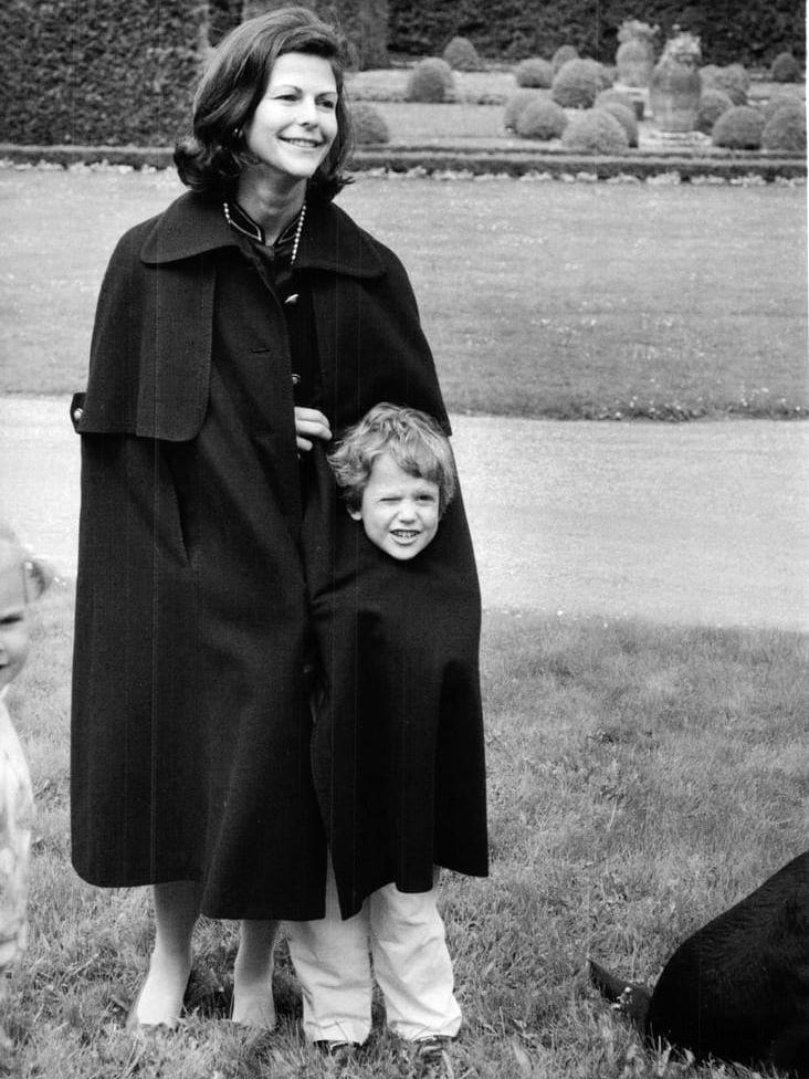 Att ständigt vara påpassad av fotografer kan nog få vem som helst att vilja gömma sig. Så verkar prins Carl Philip tycka när han gömde sig under mammas stora kappa vid en fotografering på Solliden, Öland. Året var 1984.